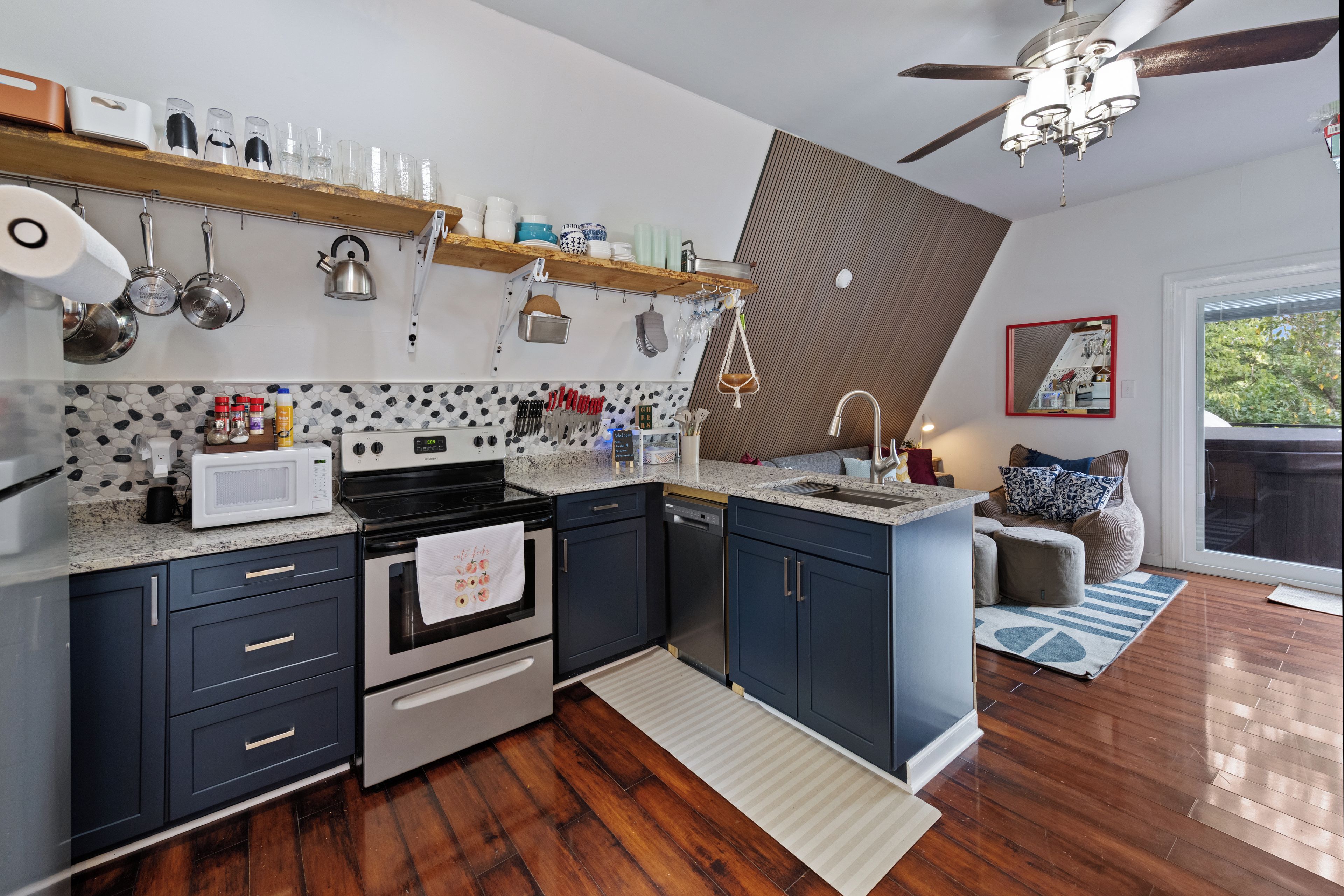 Une cuisine moderne équipée d’un four à micro-ondes, d’une cuisinière et d’un four. Le sol est en bois et il y a un ventilateur au plafond.