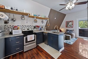Une cuisine moderne équipée d’un four à micro-ondes, d’une cuisinière et d’un four. Le sol est en bois et il y a un ventilateur au plafond.