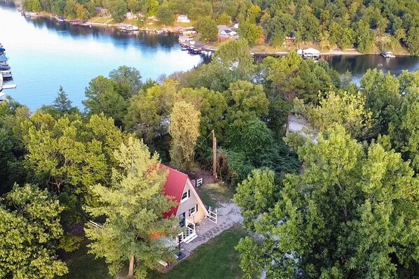 Una propiedad junto al lago con una cabaña de techo rojo, rodeada de árboles densos y barcos amarrados.