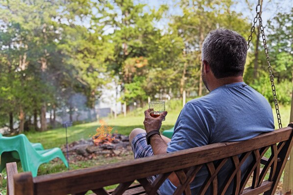 A person sitting on a wooden swing with a fire in the background.