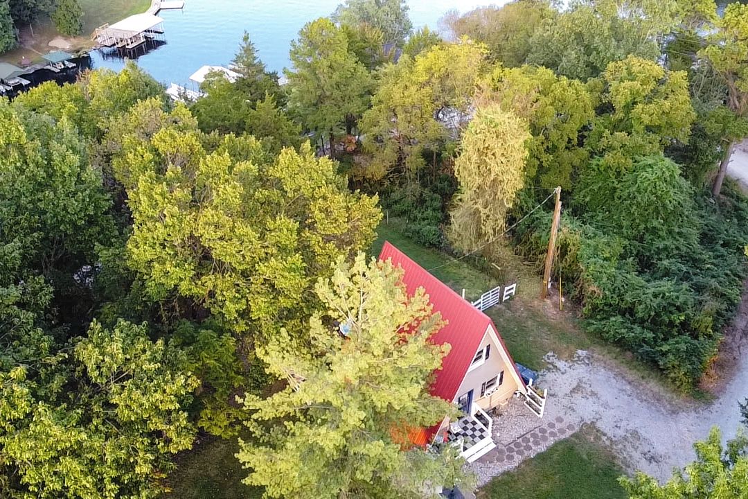 Une maison avec un toit rouge, entourée d’une végétation luxuriante, et une jetée qui s’avance dans un plan d’eau.