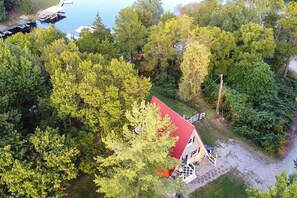 A house with a red roof surrounded by dense greenery and a dock extending into a body of water.