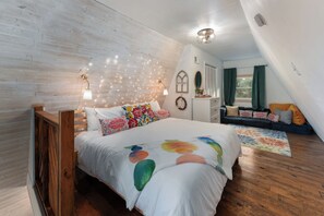 A bedroom with a wooden bed, a nightstand, a dresser, a window with curtains, and a wall-mounted light fixture.