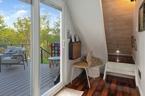 A room with a sliding glass door leading to an outdoor deck, a small table with a chair, a wooden chair, and a white bench.