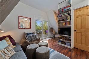 A cozy living room with a sectional sofa, ottomans, a bookshelf, and a television.