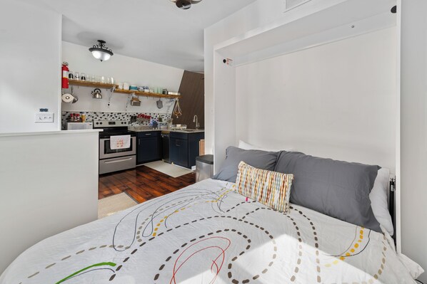 A bedroom with a bed, pillows, and a view into a kitchen area.