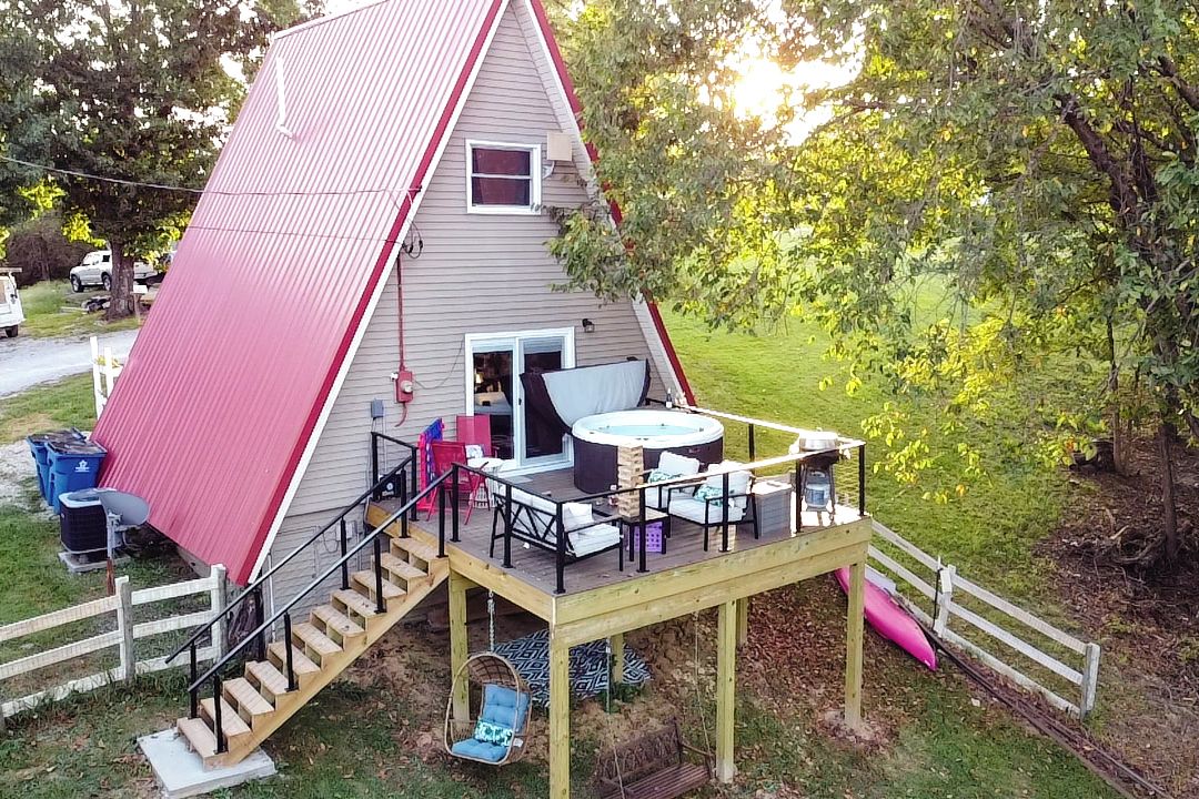A triangular house with a deck, a hot tub, and outdoor seating.