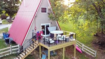 A triangular house with a deck, a hot tub, and outdoor seating.