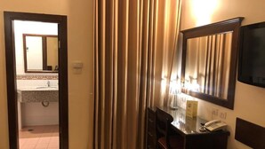 A hotel room with a desk, chair, and a large mirror. There is a bathroom visible through an open door.