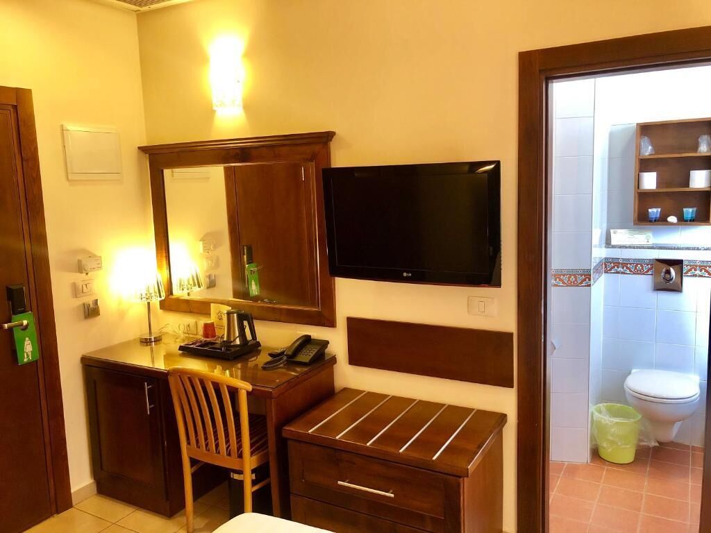 A hotel room with a desk, chair, TV, and a small bathroom with a toilet and shelves.