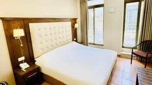 A hotel room with a large bed, a nightstand, a chair, and a window.