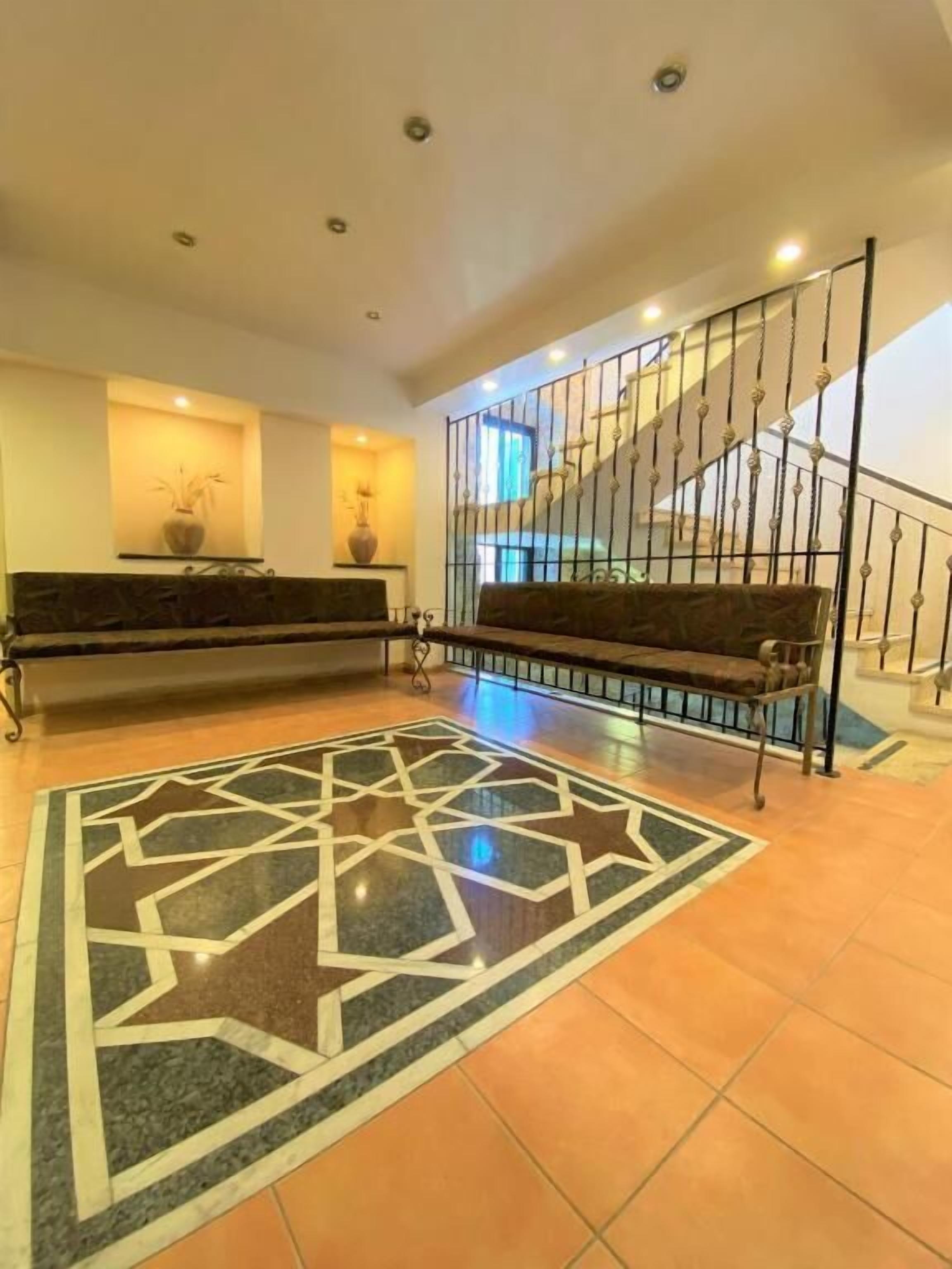 A hotel lobby with a patterned carpet, a reception desk, a staircase, and a railing.