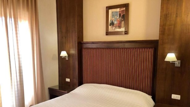 A hotel room with a large bed, wooden headboard, two bedside tables with lamps, and a painting on the wall.