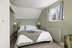 A bedroom with a bed, bedside lamps, a window with curtains, and a radiator. - Thomas Street House -  a cottage that sleeps 6 guests  in 3 bedrooms (Cirencester)