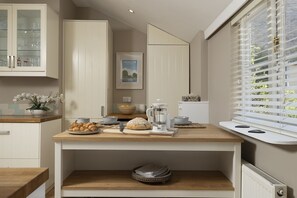 Een keuken met een houten aanrecht, een koffiezetapparaat, een brood en een raam met jaloezieën.