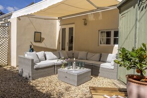 Ein überdachter Außenbereich mit Korbmöbel-Sofa und Tisch, umgeben von Kies.