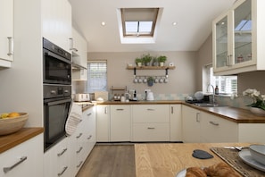 A modern kitchen with a skylight, built-in ovens, a wooden countertop, and a breakfast bar. - Thomas Street House -  a cottage that sleeps 6 guests  in 3 bedrooms (Cirencester)