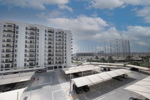 A multi-story residential building with balconies, a parking area with covered parking spaces, and a large stadium in the background. - Bloomfields 2BR in Waters Edge 9  (Abu Dhabi)