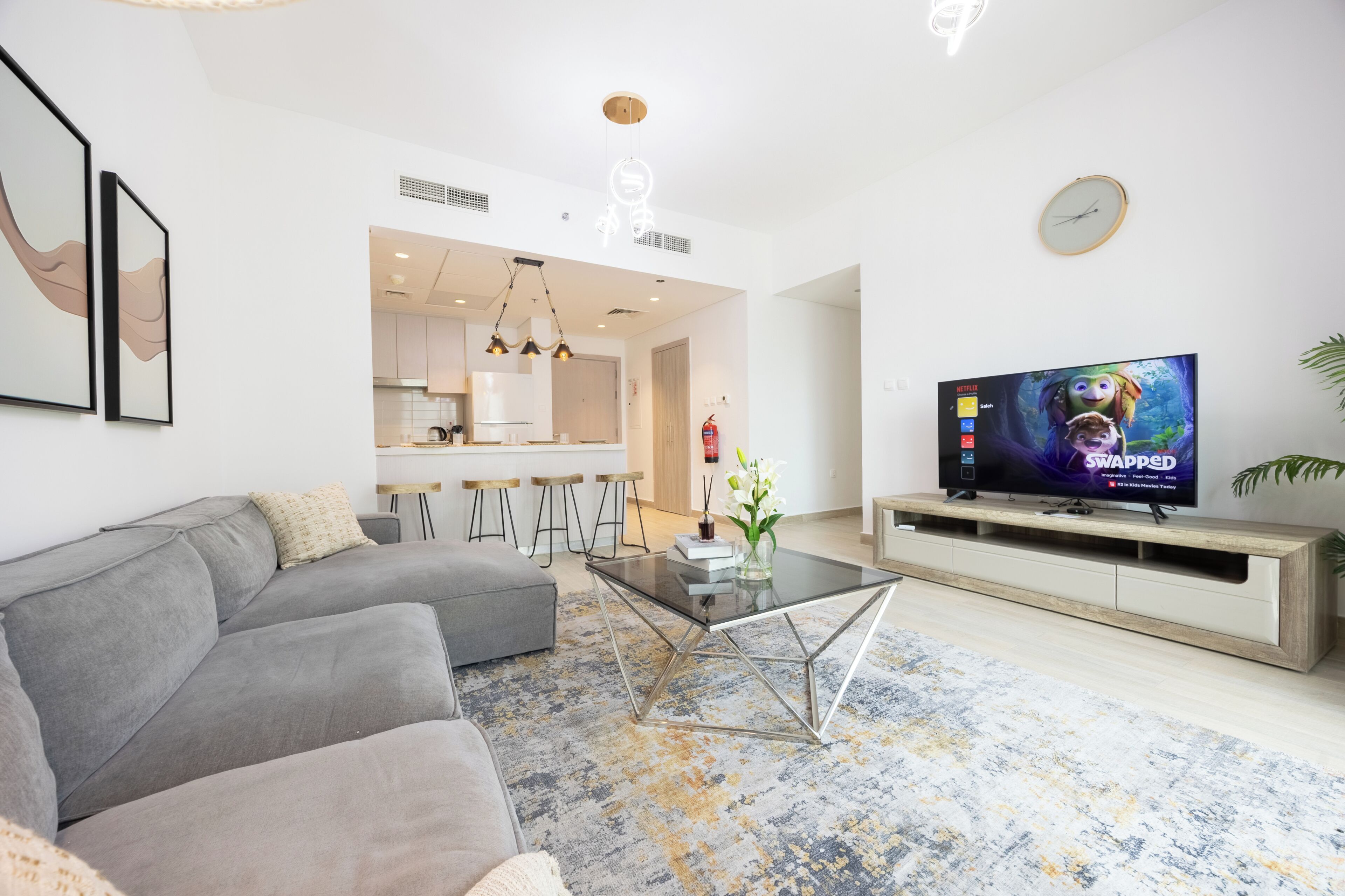 Una sala de estar moderna con un sofá gris, una mesa de centro y un televisor de pantalla plana sobre un soporte de madera.