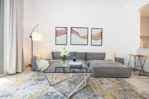 A modern living room with a glass coffee table, grey sectional sofa, and abstract wall art. - Bloomfields 2BR in Water's Edge B9-Yas Island (Abu Dhabi)