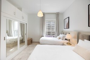 A hotel room with a large bed, a bedside table with a lamp, a mirror, and a view of a building through the window. - Bloomfields 2BR in Waters Edge 9  (Abu Dhabi)