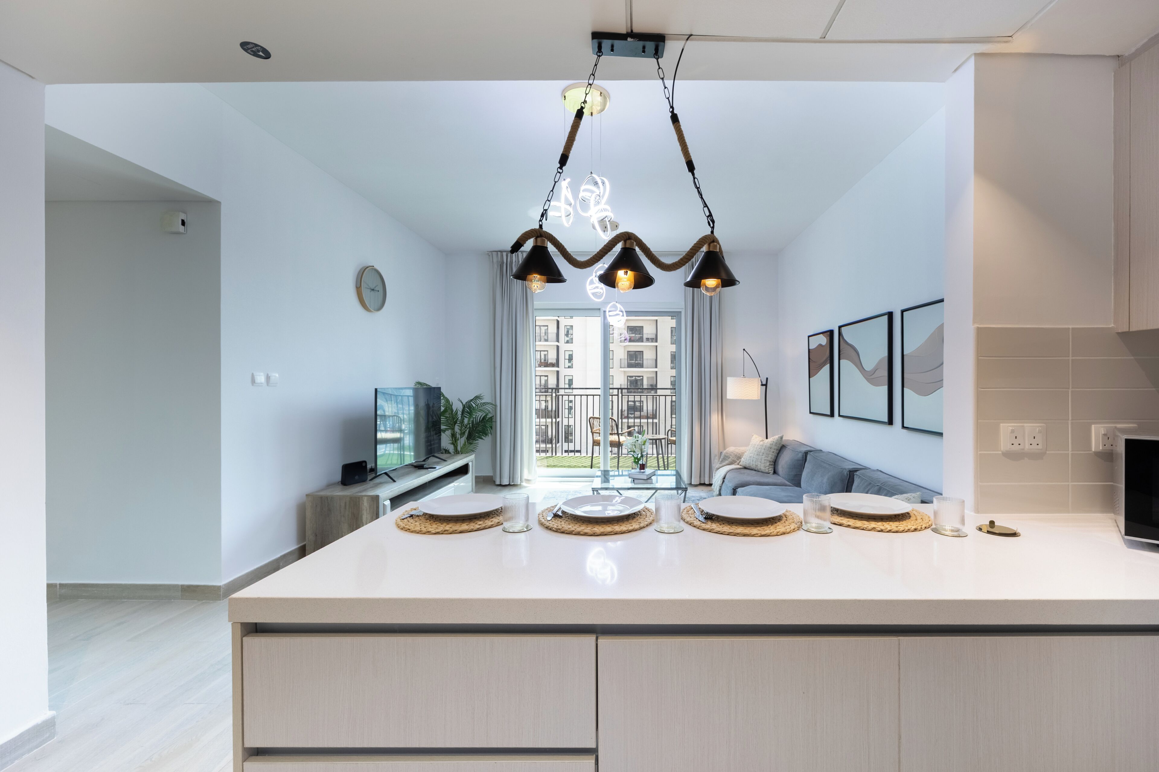 A modern kitchen with a central island, pendant lighting, and a view to an outdoor balcony.