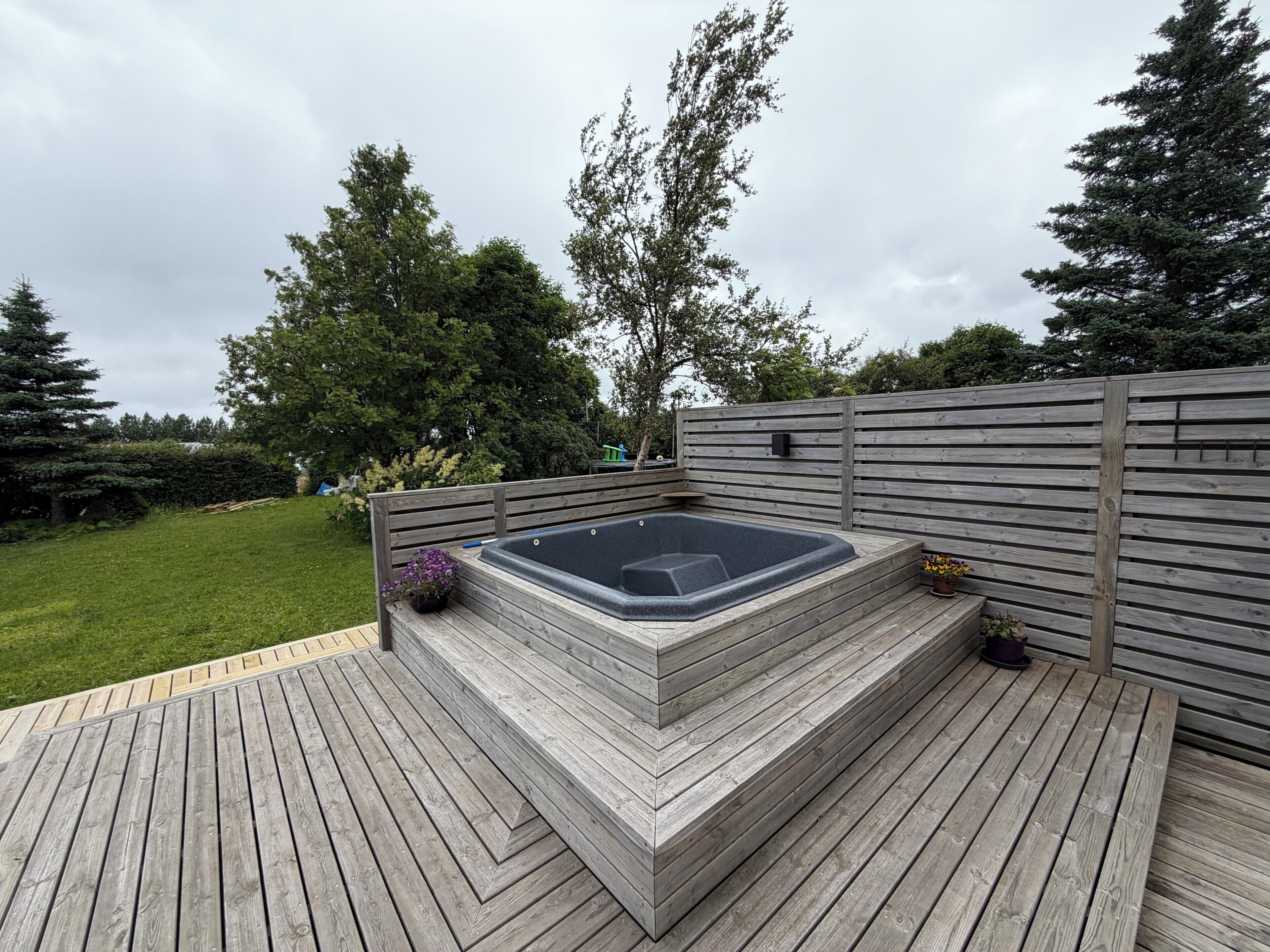 A hot tub on a wooden deck with a wooden fence and trees in the background.
