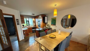 A modern kitchen with wooden cabinets, a central island, and a dining area with a wooden table and chairs. - Modern family friendly house in Reykjavik area (Garðabær)