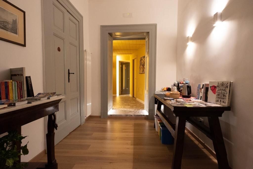 A hallway with a wooden floor, a door on the left, and a table with various items on the right.