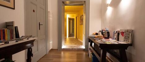 A hallway with a wooden floor, a door on the left, and a table with various items on the right.