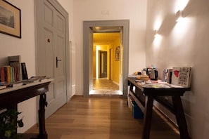 A hallway with a wooden floor, a door on the left, and a table with various items on the right. - o Panar al Duomo (Naples)