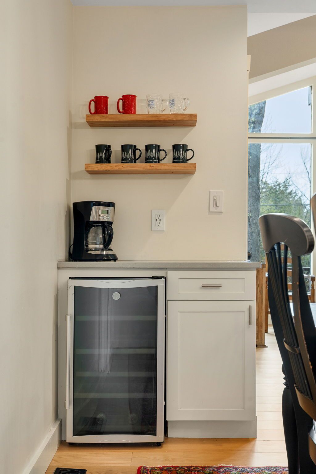 A compact kitchen with a refrigerator, coffee maker, and mugs on shelves.