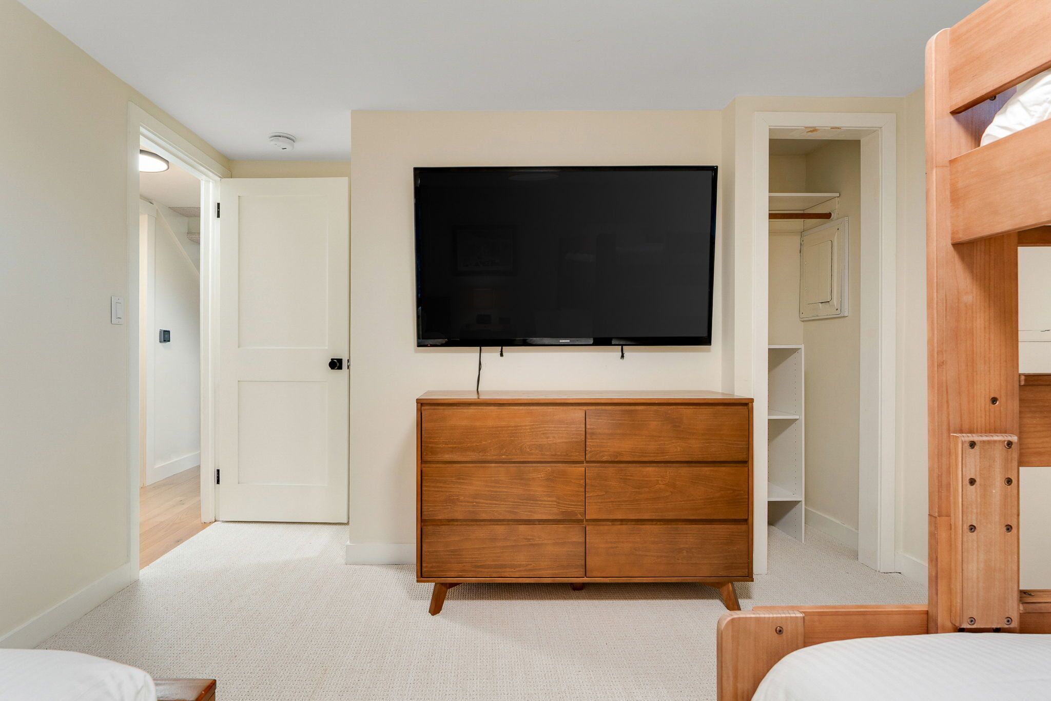 A bedroom with a TV mounted on the wall, a wooden dresser, a closet, and a bunk bed.