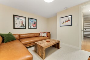 A room with a brown leather sofa, a wooden coffee table, and two framed posters on the wall. - Renovated Modern Chalet in Mad River Valley (Warren)
