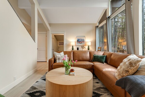A living room with a brown leather sofa, a round coffee table, and a vase of flowers.