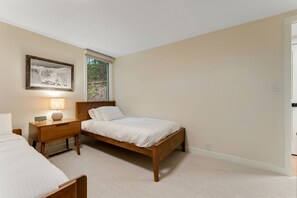 A bedroom with a single bed, a nightstand with a lamp, a framed picture on the wall, and a window with a view of trees. - Renovated Modern Chalet in Mad River Valley (Warren)