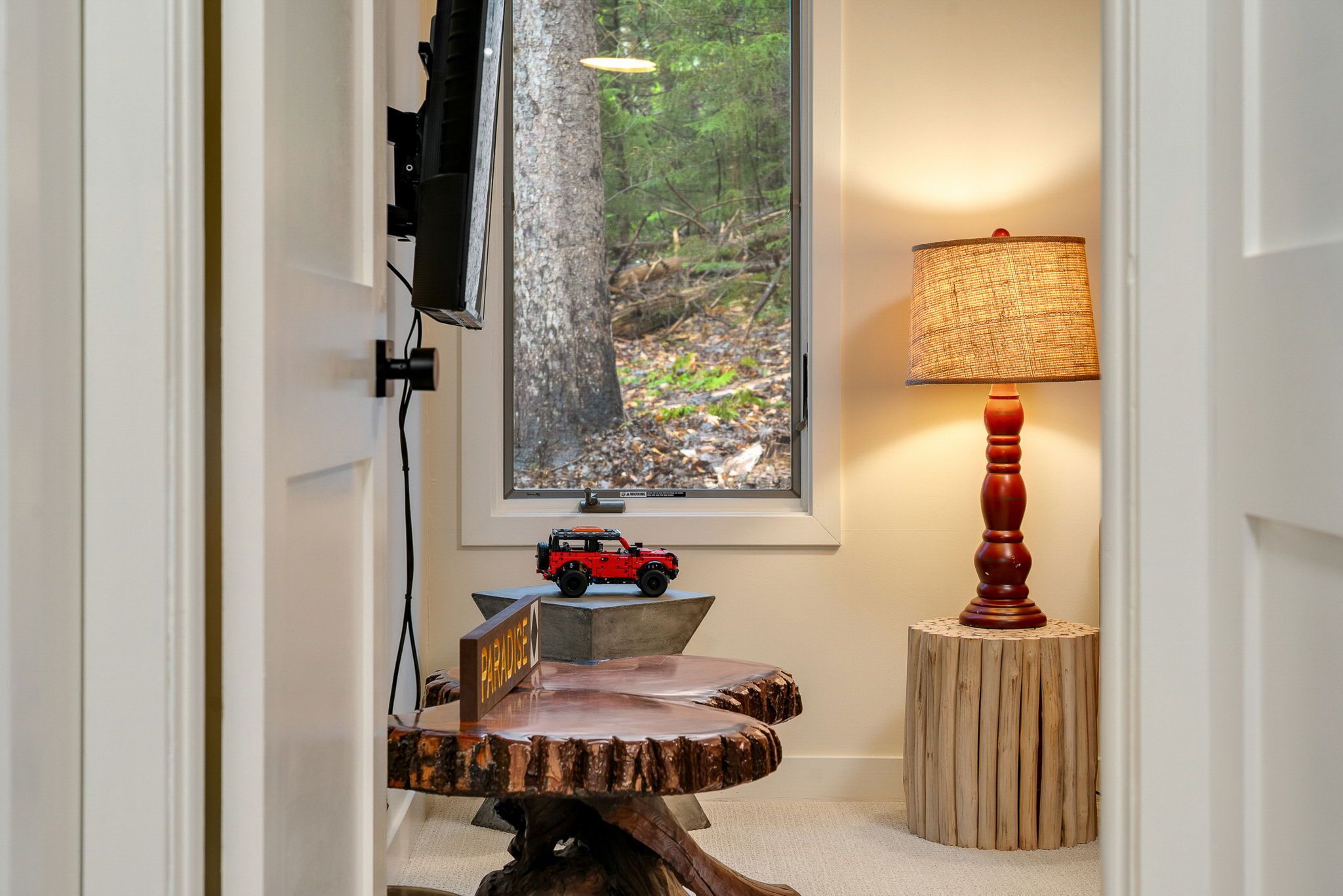 Una mesa de comedor de madera con un letrero que dice 'PARADISE', una lámpara y un coche de juguete sobre un pedestal.