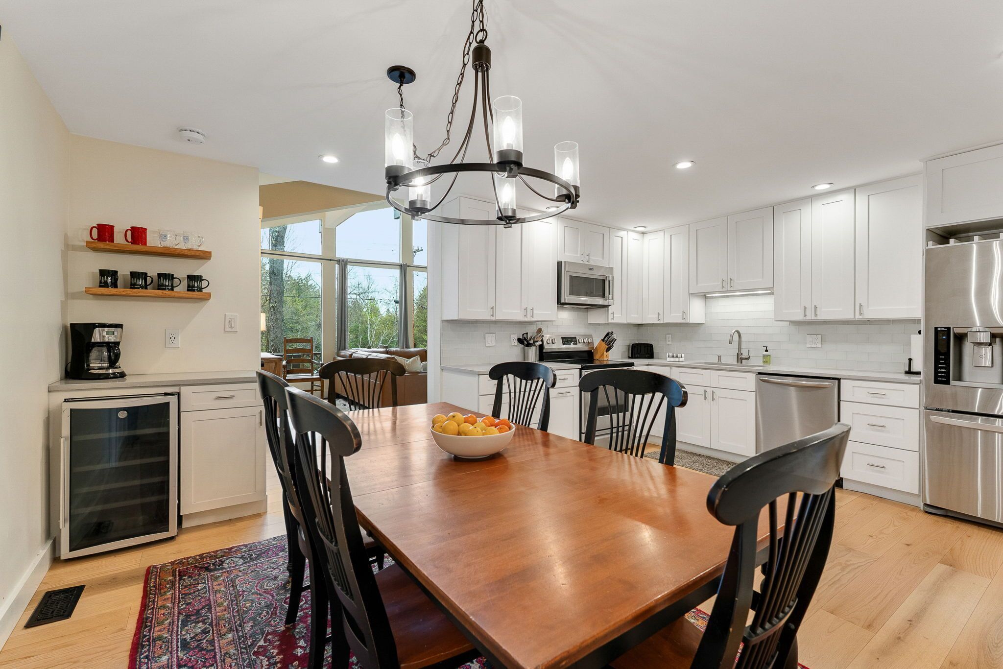 A modern kitchen with white cabinets, stainless steel appliances, and a wooden dining table with chairs.