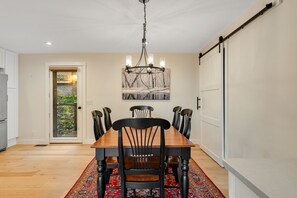 A dining room with a wooden table, black chairs, a chandelier, and a red patterned rug.