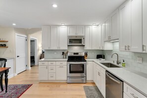 A modern kitchen with white cabinetry, stainless steel appliances, and a wooden dining table.
