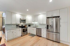 A modern kitchen with white cabinets, stainless steel appliances, and a wooden floor. - Renovated Modern Chalet in Mad River Valley (Warren)