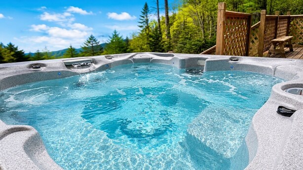 Ein Whirlpool mit Steinfassade, umgeben von einer Holterrasse und Bäumen.