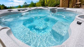 Un jacuzzi con revestimiento de piedra, rodeado por una terraza de madera y árboles.