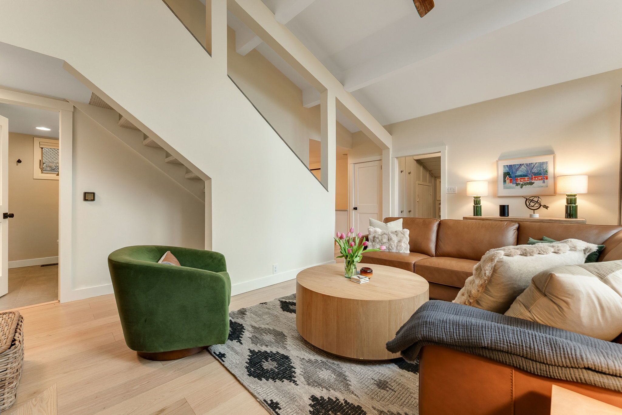 Een moderne woonkamer met een trap, een groene fauteuil, een bruine bank en een ronde salontafel.