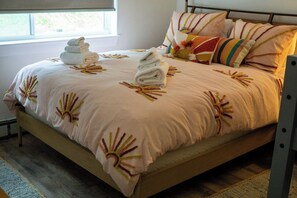 Ein Bett mit blumigem Überwurf, Kissen und gefalteten Handtüchern.