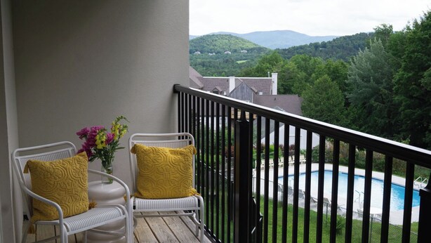 A balcony with two wicker chairs, a small table, and a vase with flowers. - 1BR, 2nd Floor Condo at Sugarbush (Warren)