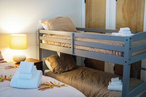 Ein Etagenbett mit zwei Schlafstellen, ein Nachttisch mit Lampe und ein ordentlich bezogenes Bett mit Handtüchern.