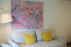 Ein Wohnzimmer mit einem hellen Sofa, zwei gelben Zierkissen, einem modernen abstrakten Gemälde und einer Stehlampe.