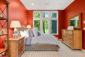 Een slaapkamer met een groot bed, een kaptafel, een nachtkastje en een raam met uitzicht op bomen.