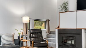 Ein Wohnzimmer mit einer Couch, einem Holztisch, einem Ledersessel, einem Kamin und einem Fenster mit Vorhängen.